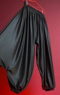 Black satin pants on a red hanger against a red background